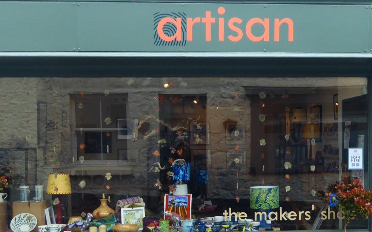 Artisan, Chagford (photo by Artisan) Photograph of the Artisan shop front with a large window filled with pictures, lamps, bowls and handmade items