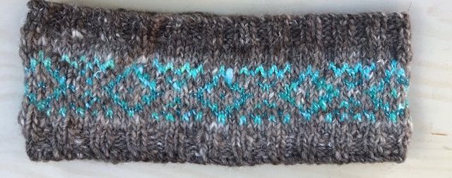 A knitted headband in natural grey yarn with a turquoise diamond shaped pattern across the middle