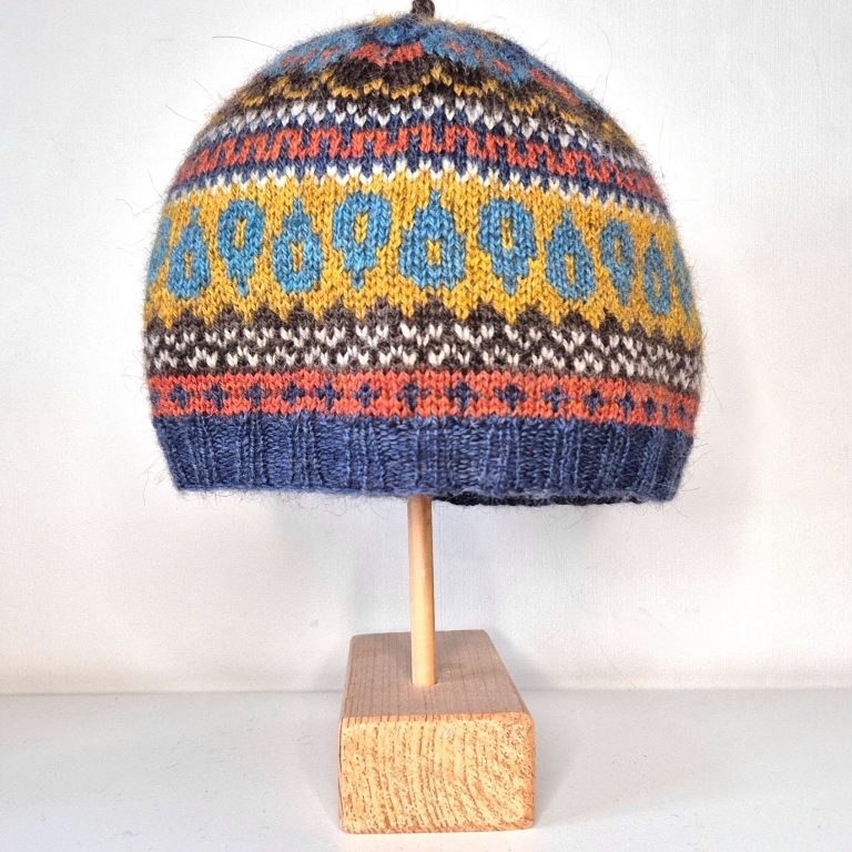 A Fair Isle hat with stripes of blue, orange, brown and yellow with repeating motifs on each in orange, cream and pale blue